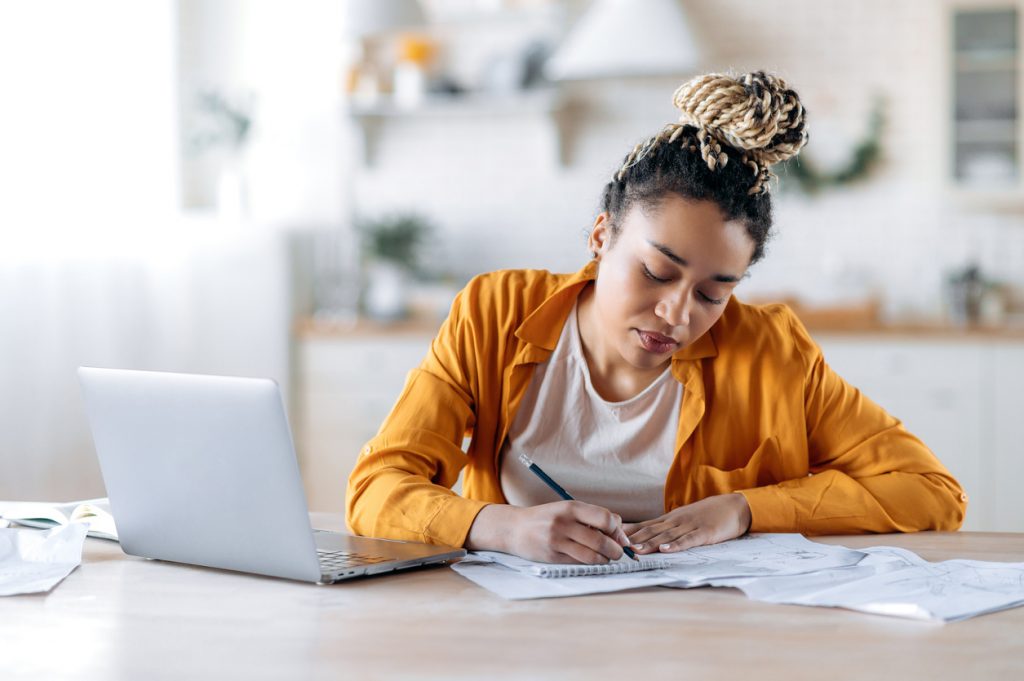 A female student sits at a desk with papers and a laptop